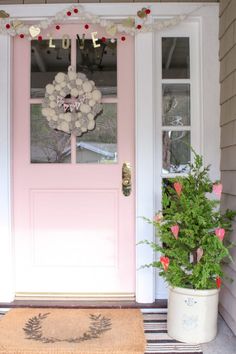 a pink front door with a wreath and potted plants on the porch next to it