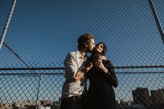 two people standing next to each other near a fence