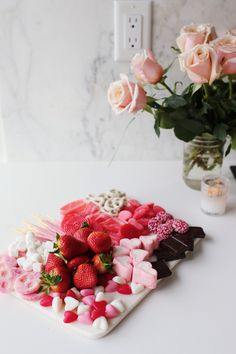 a plate with strawberries and marshmallows on it next to a vase filled with roses