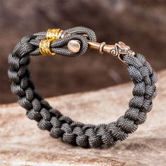 a black and gold braided bracelet with two metal beads on the end, sitting on top of a rock