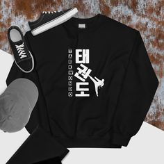 Taekwondo is written in Korean, and a male is kicking one of the letters to a tilt! Fun and expressive shirt for the TKD athlete, enthusiast, lover or supporter! A sturdy and warm sweatshirt bound to keep you warm in the colder months. A pre-shrunk, classic fit sweater that's made with air-jet spun yarn for a soft feel and reduced pilling. * 50% cotton, 50% polyester * Pre-shrunk * Classic fit * 1x1 athletic rib knit collar with spandex * Air-jet spun yarn with a soft feel and reduced pilling * Hip Hop Style Letter Print Sweatshirt For Sports, Hip Hop Letter Print Sweatshirt For Sports Events, Black Sports Sweatshirt With Text Print, Black Sporty Sweatshirt With Name Print, Sporty Black Sweatshirt With Name Print, Sporty Sweatshirt With Screen Print For Sports, Sporty Crew Neck Sweatshirt For Training, Casual Crew Neck Sweatshirt For Training, Taekwondo Shirt