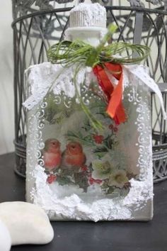 a glass bottle with flowers on it sitting in front of a birdcage filled with leaves and berries