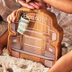 two people are holding a wooden sign with money in the shape of a truck on it