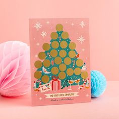 a card with a christmas tree on it next to two balls of yarn and a ball of pom - poms