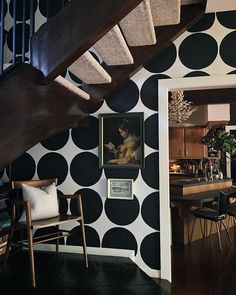 a living room with black and white polka dots on the wall, stairs leading up to an open kitchen area