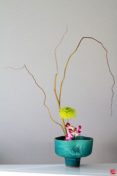 a blue vase with flowers in it on a white countertop against a gray wall