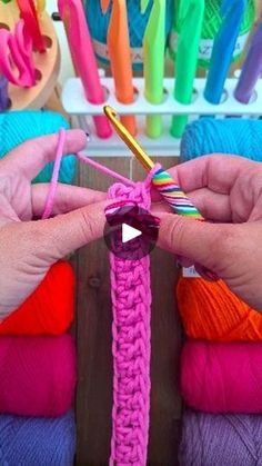 two hands holding yarn and crochet hooks in front of colorful balls of yarn