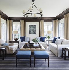 a living room with couches, chairs and tables in front of two large windows