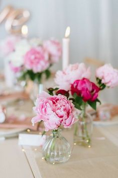 pink peonies in vases on a table with candles and napkins around them