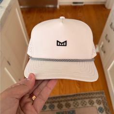 a person holding up a white hat with the word m on it in front of a kitchen