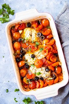 a casserole dish filled with tomatoes, olives and cheese on a blue surface