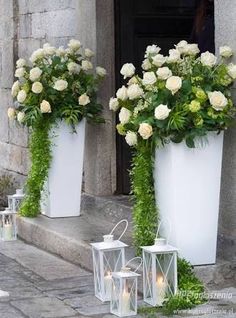 three white vases filled with flowers and greenery on the side of a building