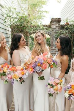 a group of women standing next to each other holding bouquets in front of a house