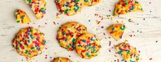 sprinkle covered cookies are arranged on a white wooden surface with colorful sprinkles