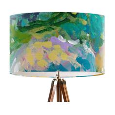 a colorful lamp shade on a tripod shaped wooden base with an abstract painting in blue, green and yellow