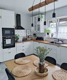 a kitchen with white cabinets and wooden table surrounded by black chairs, potted plants on the counter