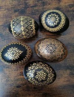 four black and gold painted rocks on a wooden table