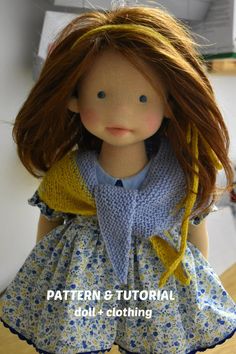 a doll with red hair wearing a blue dress and yellow scarf over her head, sitting on a table