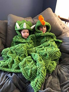 two children in green crocheted costumes laying on a bed with pillows and blankets