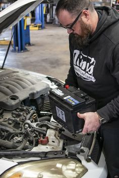 a man working on a car engine in a garage with the hood up and it's hood open