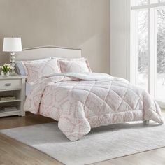 a bed with pink and white comforter in a bedroom next to a window on top of a rug