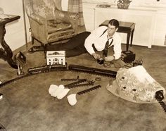 a man sitting on the floor next to a model train set and other items in front of him