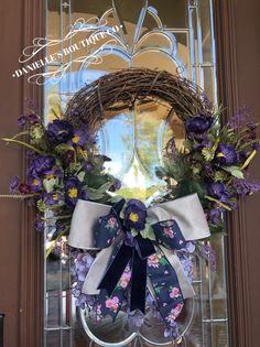 a wreath with purple and white flowers is hanging on the front door to welcome guests