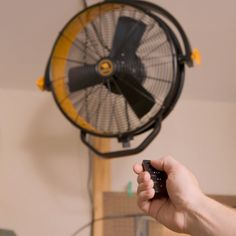 a person holding a remote control in front of a fan