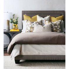 a bed with yellow and gray pillows on it's headboard next to a night stand