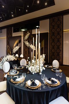 a table set with black linens and white flowers, gold trimmings and candles