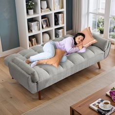 a woman laying on top of a gray couch in a living room next to a window