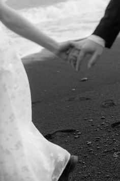 the bride and groom are holding hands on the black sand at the ocean's edge