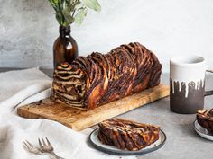 a loaf of chocolate cake sitting on top of a wooden cutting board next to a cup