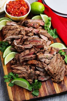 sliced up steak on a cutting board with salsa and limes