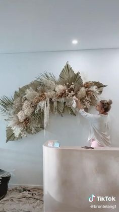 a woman standing in front of a white counter next to a wall with flowers on it