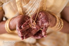 a woman holding her hands with henna tattoos on it's palms and wearing gold jewelry