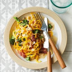 a white plate topped with pasta and broccoli next to a glass of water