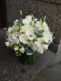 a bouquet of white flowers sitting on top of a stone floor next to a wall