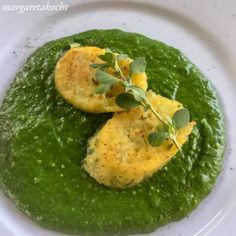 two omelets on a white plate covered in green pesto sauce and garnished with fresh herbs