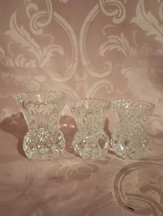 three clear glass vases sitting on top of a pink cloth covered bed spreader