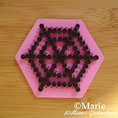 a pink tray with black beads in the shape of a flower on top of a wooden table