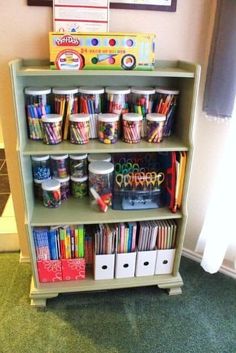 a green book shelf filled with children's books and craft supplies next to a window