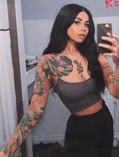 a woman with tattoos taking a selfie in the mirror while holding her cell phone