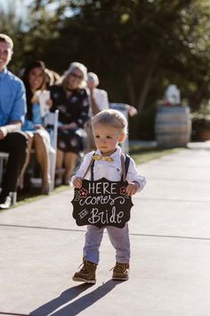 a little boy holding a sign that says here comes the bride and is ready to walk down the aisle