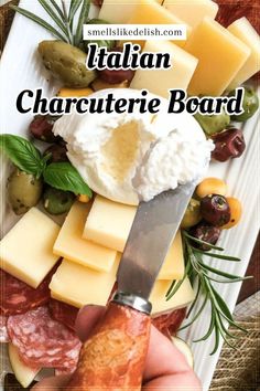 a person holding a knife over cheese and meats on a plate with the words italian charcuterie board