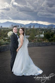 a bride and groom pose for a photo in front of the city skyline on their wedding day