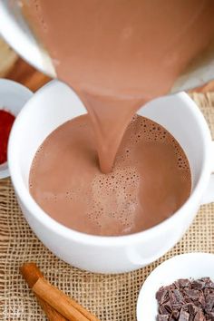 chocolate being poured into a white cup with cinnamons and spices around it on a burlap surface