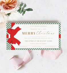 a merry christmas gift certificate next to some pink flowers and ribbon on a white surface