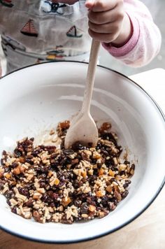 a child holding a wooden spoon in a bowl filled with rice and raisins