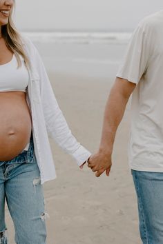 a pregnant woman holding her husband's hand on the beach while they hold hands